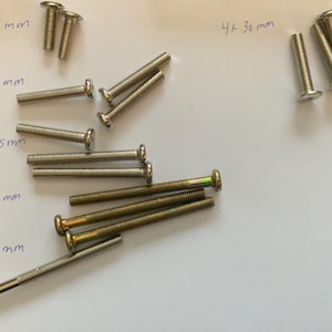 May include: A collection of screws in various sizes, including 2x20 mm, 4x35 mm, 2x55 mm, 3x70 mm, and 1x75 mm. The screws are silver and gold in color.