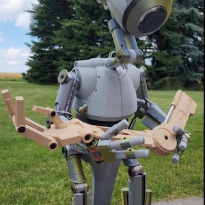 May include: A grey and brown articulated robot with a large head and jointed arms and legs. The robot is standing on a grey surface.