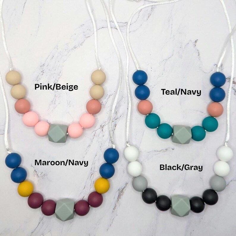 Puede incluir: Cuatro collares de cuentas de silicona de colores con cordones blancos. Los collares est&aacute;n disponibles en las siguientes combinaciones de colores: Rosa/Beige, Turquesa/Marino, Granate/Marino y Negro/Gris. Cada collar tiene una cuenta geom&eacute;trica gris en el centro.