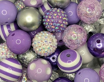May include: A collection of purple and silver beads, some with white polka dots or stripes. The beads are made of various materials, including plastic, glass, and metal.