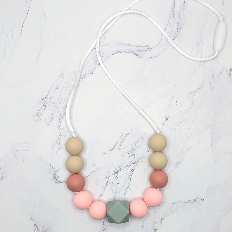Puede incluir: Un collar con cuentas rosas, beige y verdes. El collar tiene un cord&oacute;n blanco y un cierre blanco. Las cuentas son redondas, con una cuenta geom&eacute;trica en forma de cubo.