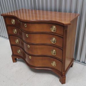 May include: A curved, wooden chest of drawers with four drawers and brass hardware. The chest is a rich brown color and has a traditional style.