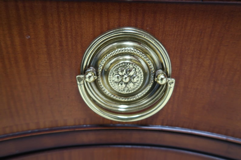 May include: A gold-toned drawer pull with a decorative floral design. The pull is mounted on a wooden surface.