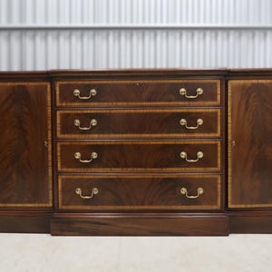May include: A dark wood sideboard with four drawers and two cabinet doors. The drawers and doors have decorative trim and brass-colored handles. The wood grain is visible throughout the piece, and the overall design is traditional.