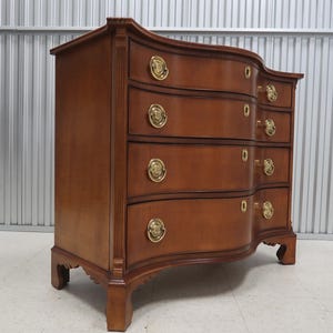 May include: A curved, wooden chest of drawers with four drawers and brass hardware. The chest is made of a rich, dark wood and has a traditional design.