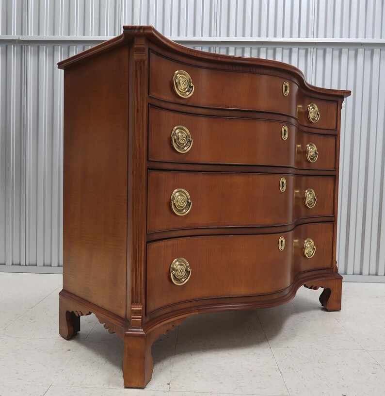 May include: A curved, wooden chest of drawers with four drawers and brass hardware. The chest is made of a rich, dark wood and has a traditional design.