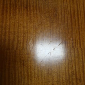 May include: A close-up of a light brown wooden surface with a subtle grain pattern. The surface has a few light scratches.