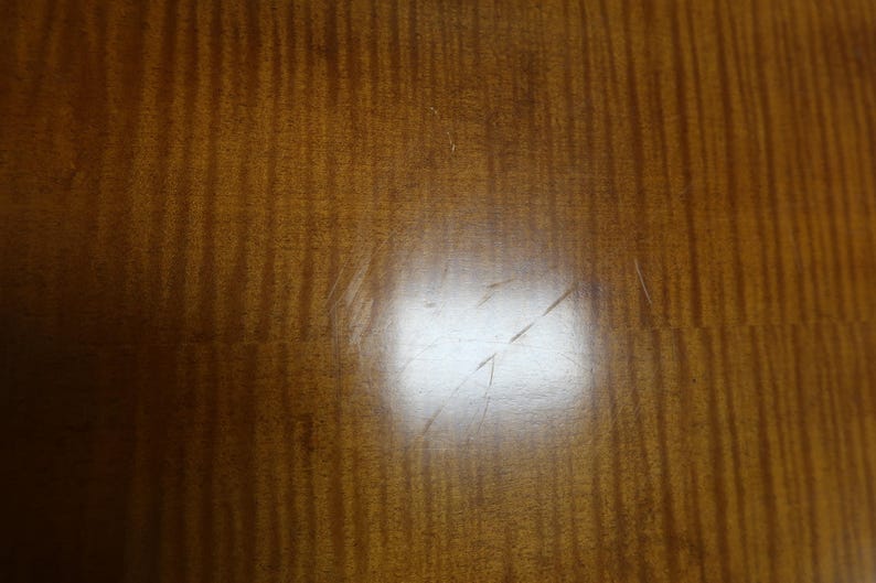 May include: A close-up of a light brown wooden surface with a subtle grain pattern. The surface has a few light scratches.