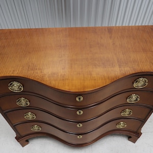 May include: A four-drawer chest of drawers with a curved front and brass hardware. The chest is made of wood with a light brown finish.