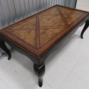 May include: A brown wood coffee table with a black painted base and intricate carved legs. The top of the table has a geometric pattern of inlaid wood.