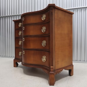 May include: A curved, wooden chest of drawers with six drawers and brass hardware. The chest is made of a rich, dark wood with a warm, natural finish.