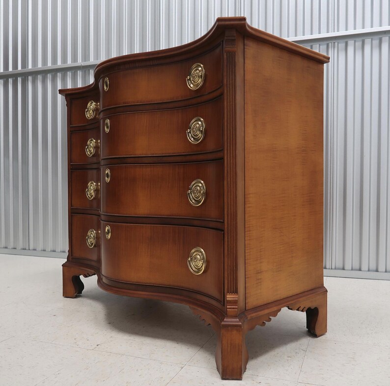 May include: A curved, wooden chest of drawers with six drawers and brass hardware. The chest is made of a rich, dark wood with a warm, natural finish.