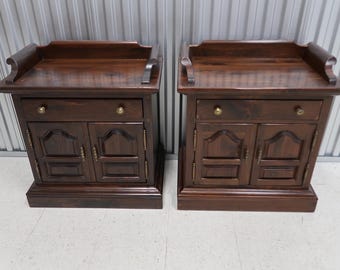 Puede incluir: Dos mesitas de noche de madera marrón oscuro a juego con un cajón y dos puertas. Cada mesita de noche tiene un borde superior decorativo y herrajes de latón.