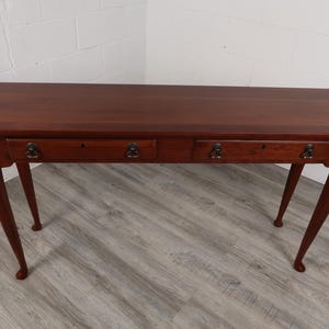 May include: A dark brown wooden desk with two drawers and four slender, curved legs. The desk has a rectangular top and antique-style drawer pulls. The desk is made of wood and has a polished finish.