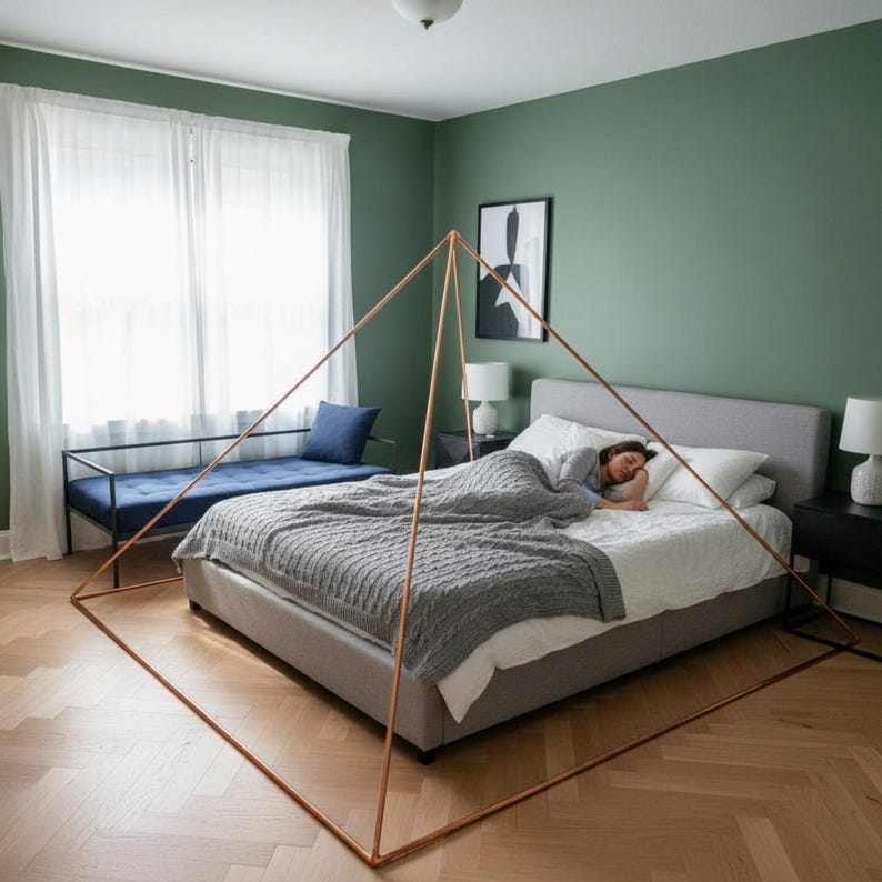 May include: A large, geometric, copper-colored metal pyramid frame structure positioned around a bed. The frame consists of thin, straight rods that meet at a single apex point above the center of the bed, creating a distinct triangular silhouette.