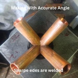May include: A copper pipe fitting with four cylindrical arms arranged in an X-shape, featuring welded joints at the centre. The text "Making With Accurate Angle" and "Sharpe edes are welded" is visible on the image surface.