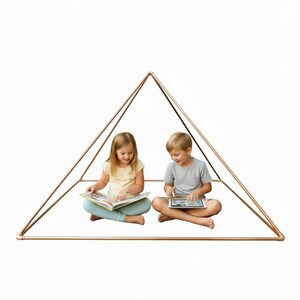 May include: A pyramid-shaped frame constructed from metallic copper-colored pipes. The structure features a square base and four angled sides meeting at a single top point, creating an open, geometric enclosure for indoor play or reading activities.