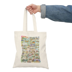 May include: A white canvas tote bag with a colorful illustration of La Jolla, California. The illustration includes buildings, landmarks, and activities.