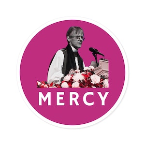 Puede incluir: Una pegatina circular rosa con la palabra "MERCY" en texto blanco. Un hombre con una túnica negra y gafas habla en un podio con flores delante de él.
