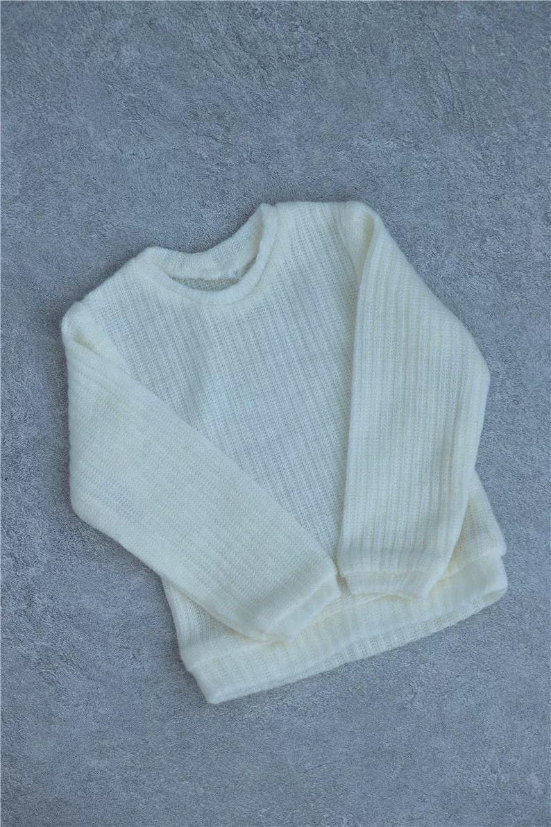 May include: Ivory-colored sweater with a crew neck and long sleeves. The knitwear has a ribbed texture and a relaxed fit. This cozy sweater is perfect for casual wear.