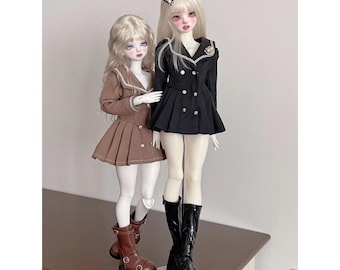 May include: Two dolls wearing brown and black dresses with white collars and buttons. The dolls are wearing brown and black boots. The dolls are standing on a wooden surface.