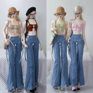 May include: Three fashion dolls wearing different coloured crop tops and denim bell bottom trousers. Each doll is wearing a straw hat and has long hair. The dolls are standing on a white surface.