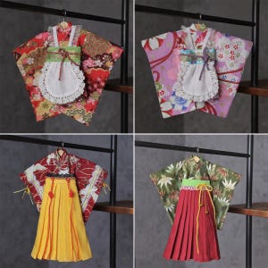 May include: Four miniature Japanese kimono outfits, each with unique patterns and colours. The kimonos are displayed on small hangers, showcasing the intricate designs and traditional elements. The outfits include a variety of colours, including red, pink, yellow, and green.