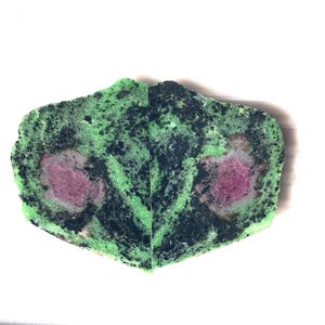 Pode incluir: Uma placa polida de mineral zoisite com uma base verde vibrante, inclusões pretas profundas e dois cristais de rubi magenta arredondados e proeminentes incrustados na pedra, apresentada como um par simétrico de seções de rocha cortada.