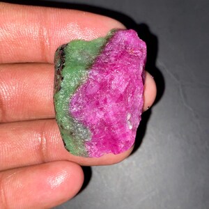 以下が含まれることがあります： 鮮やかなマゼンタピンクの中心部と、質感のある明るい緑色の外層が対照的な、未研磨の原石標本。石は不規則でギザギザした形状をしており、全体的に結晶質の粗い表面の質感が特徴です。