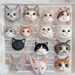 Pode incluir: Uma coleção de 13 estatuetas de cerâmica de gatos em várias poses e cores, incluindo branco, cinza, marrom, preto e laranja. As estatuetas são exibidas em um fundo de grade branca.