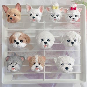 Może przedstawiać: Dziewięć figurek różnych ras psów, każda z unikalnym wyrazem twarzy i kolorem futra. Figurki są wykonane z białego, brązowego i szarego materiału i są ułożone w siatkę na białym tle.