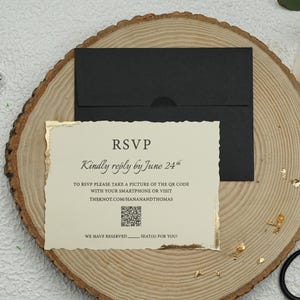May include: RSVP card with gold accents and a black envelope. The card has a QR code and the text "Kindly reply by June 24th" and "TO RSVP PLEASE TAKE A PICTURE OF THE QR CODE WITH YOUR SMARTPHONE OR VISIT THEKNOT.COM/HANANANDTHOMAS".