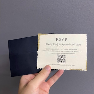 Puede incluir: Una tarjeta de confirmación de asistencia de boda con borde rasgado y ribete dorado, junto a un sobre azul marino. La tarjeta dice "RSVP Kindly Reply by September 30th, 2024" e incluye un código QR y una dirección web.