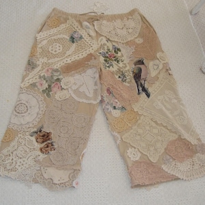 Peut inclure: Pantacourt beige avec un design patchwork. Le pantacourt est orné de divers napperons en dentelle, de patchs de tissu floral et d'une illustration d'oiseau. La palette de couleurs comprend le beige, la crème et les roses pastel, créant une esthétique vintage.