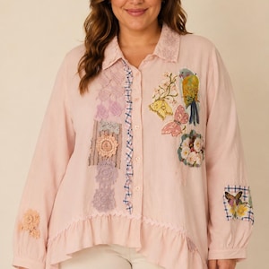 May include: A light pink long-sleeve button-down shirt featuring a ruffled hem, a blue and white checkered trim along the button placket, and various decorative patches including floral embroidery, butterflies, a parrot, and crochet lace accents.