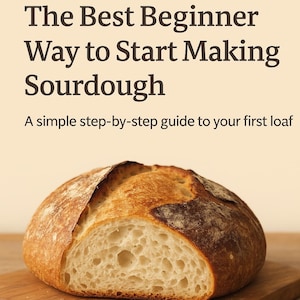 Op de afbeelding: Een in tweeën gesneden zuurdesembrood op een houten plank. Het brood heeft een knapperige, goudbruine buitenkant en een lichte, luchtige binnenkant. Bovenin staat de tekst "The Best Beginner Way to Start Making Sourdough".
