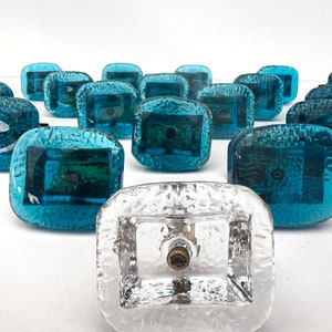 Puede incluir: Una colección de pomos de armario de vidrio azul verdoso con una superficie texturizada. Un pomo es de vidrio transparente.