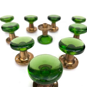 Peut inclure: Ensemble de boutons de porte anciens. Chaque bouton présente un dessus rond en verre vert transparent et une base en laiton. Les boutons sont disposés sur un fond blanc, mettant en valeur leur design et leur couleur. Ces boutons sont probablement pour les portes intérieures.