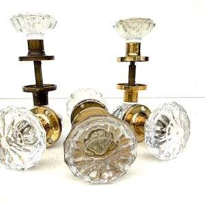 Peut inclure: Un ensemble de trois poignées de porte dotées de boutons en verre transparent à facettes avec un motif en étoile. Chaque poignée est fixée sur une base cylindrique en laiton et comprend une tige métallique et une plaque de montage circulaire.