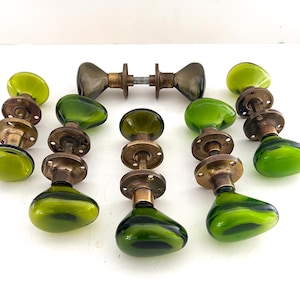 Könnte beinhalten: Eine Sammlung von Vintage-Türknöpfen mit grünem Glas und Messingbeschlägen. Die Knöpfe haben eine abgerundete Form und ein Wirbelmuster. Das Set enthält mehrere einzelne Knöpfe und ein Paar Doppelknöpfe.