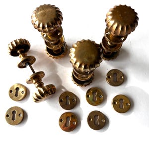 May include: A set of antique brass door furniture, featuring several door knobs with a ridged design and matching keyhole covers. The hardware has a warm, aged patina, suggesting vintage or retro styling.