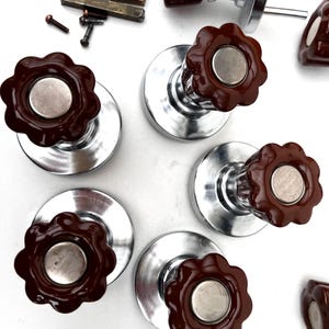 Könnte beinhalten: Eine Sammlung von Vintage-Schrankknöpfen in brauner Blütenform mit silberfarbenen Metallsockeln. Enthält auch kleine Schrauben und Metallbeschläge. Die Knöpfe haben eine glänzende Oberfläche und einen Retro-Look.