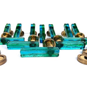 Op de afbeelding: Een verzameling vintage deurbeslag, waaronder messing sleutelgatdeksels en aqua blauwe en groene glazen deurgrepen. De handgrepen hebben een rechthoekige vorm en zijn gemonteerd op messing bases. De sleutelgatdeksels zijn rond en van messing.
