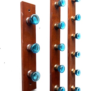 Pode incluir: Três cabides de parede de madeira com botões de vidro azul. Os cabides são feitos de madeira marrom escura e têm ferragens de cor latão. Cada cabide tem um número diferente de botões, de três a sete.