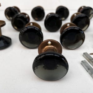 Pode incluir: Uma coleção de puxadores de porta vintage com vidro preto e ferragens de latão. Os puxadores têm formato arredondado e um gradiente de preto a cinza. Várias peças de hardware também estão presentes.