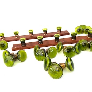Op de afbeelding: Een set van 20 groene glazen deurknoppen met messing beslag. De knoppen zijn gerangschikt op twee houten strips.