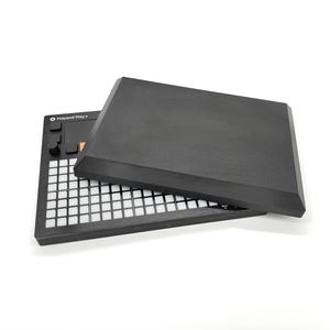 Pode incluir: Um dispositivo de produção musical Polyend Play preto com uma grade de botões brancos e uma capa preta. O dispositivo possui uma série de botões pretos e uma tela pequena. A capa está ligeiramente entreaberta.