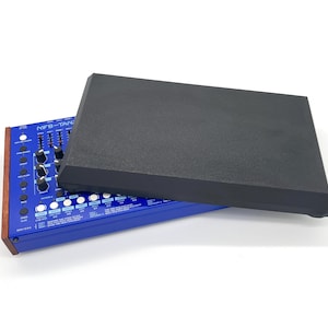 May include: A blue synthesizer with knobs and sliders, partially covered by a black rectangular cover. The synthesizer has a wooden trim and the text "MFB-Tanz" is visible.