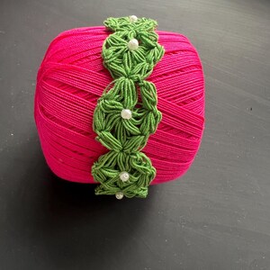 May include: A pink ball of yarn with a green crocheted trim and white beads.