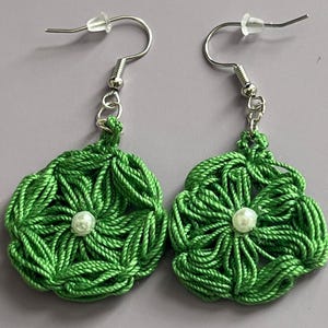 May include: A pair of green crocheted flower earrings with a white pearl bead in the center of each flower.